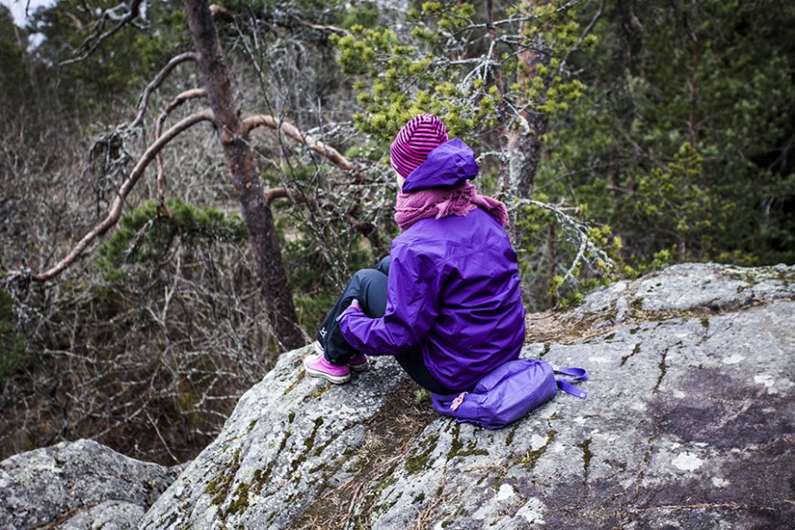 tyttölapsi istuu kalliolla metsässä