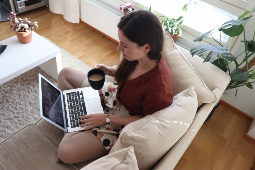 Opiskelija istumassa kotonaan läppäri sylissä ja kahvikuppi kädessä.