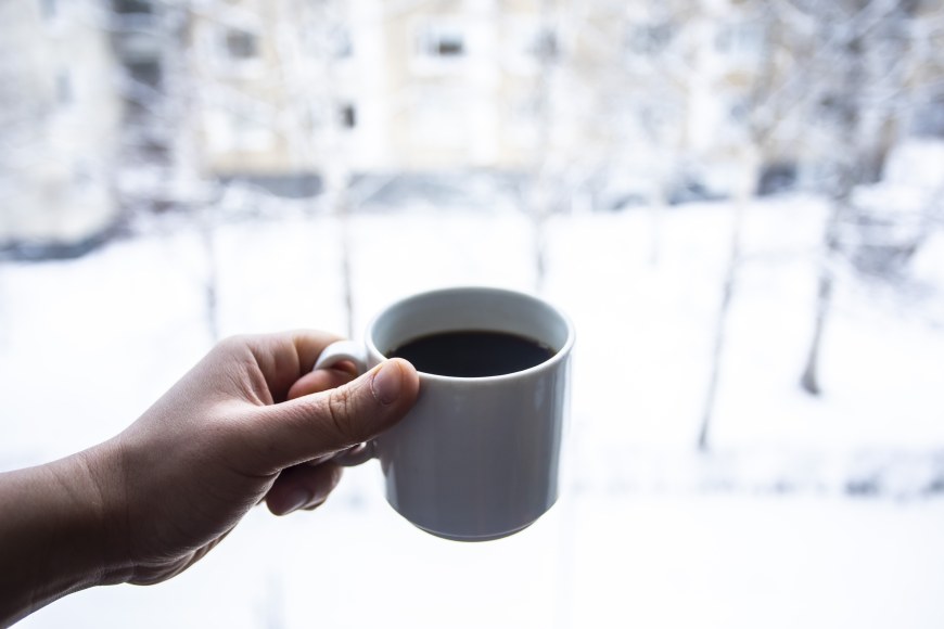 A hand holding a coffee cup against a snowy background