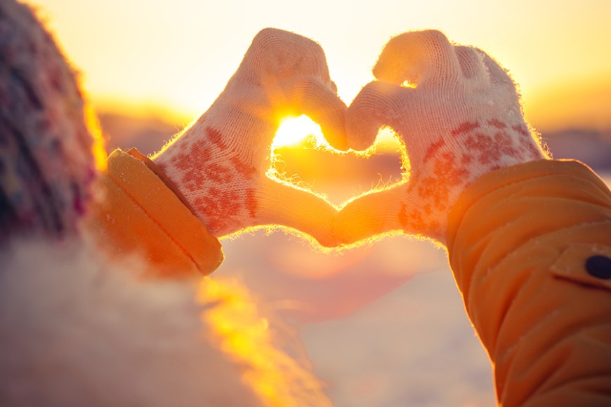 Sydämen muotoon laitetut kädet, taustalla aurinko ja talvinen maisema.