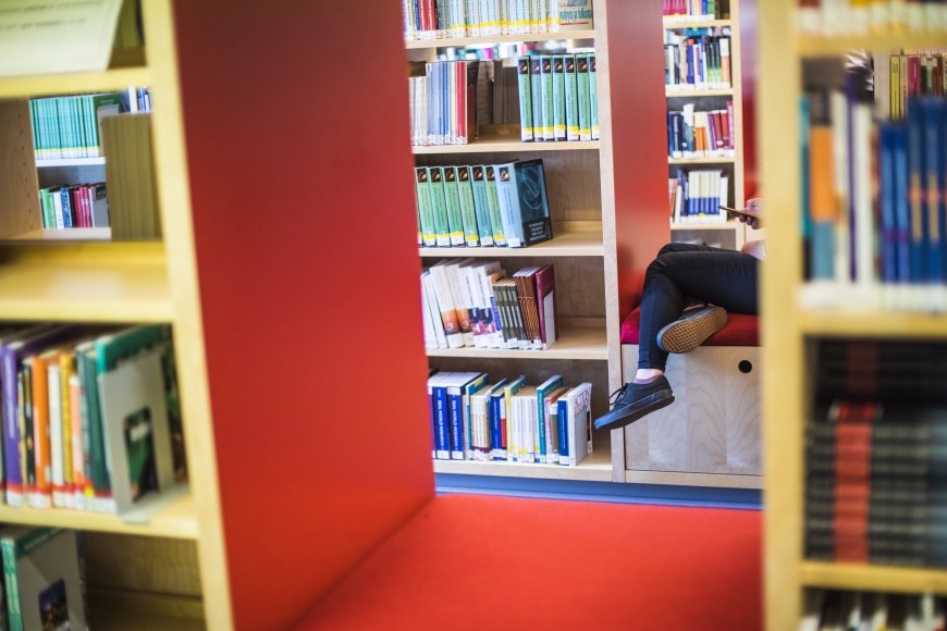 Opiskelija istumassa kirjaston hyllyjen välissä.
