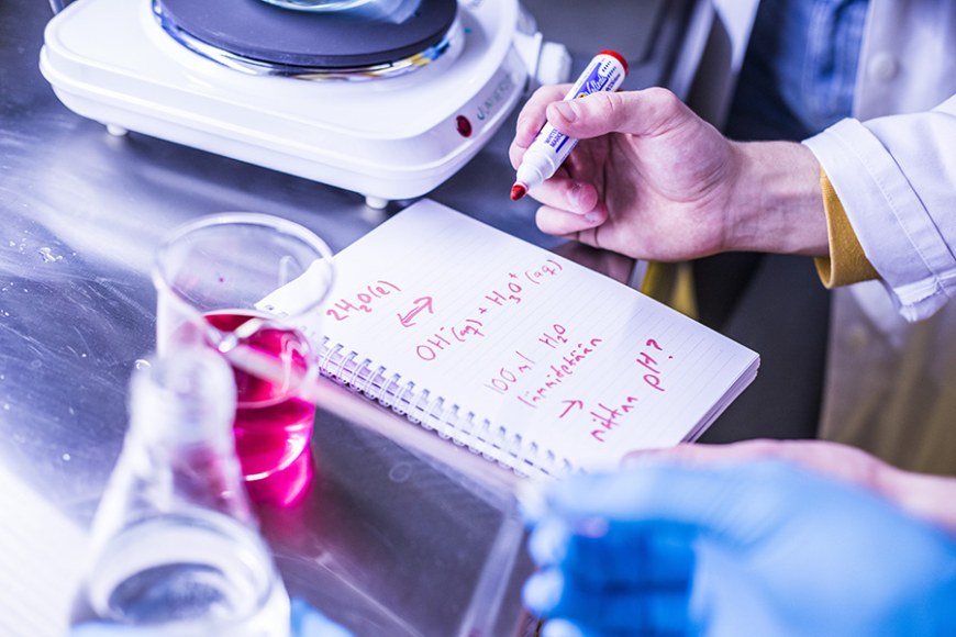 Close-up of a student taking notes in a lab setting.
