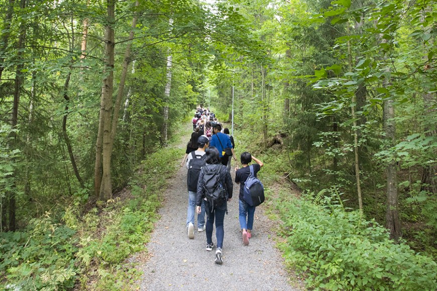 Opiskelijoita kävelemässä reput selässä metsässä.