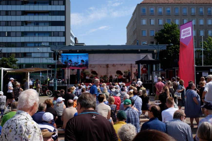 Väkijoukko on kerääntynyt aurinkoisena päivänä kuulemaan SuomiAreenan lavalla käytävää keskustelua.