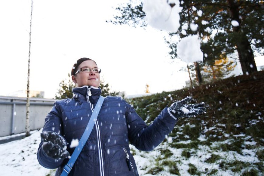 Nainen toppatakissa heittää lunta ilmaan.