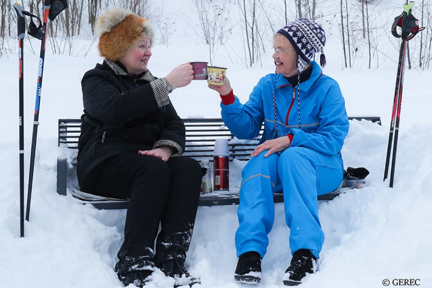 kaksi vanhaa naista istuu talvella penkillä juomassa kahvia termospullosta