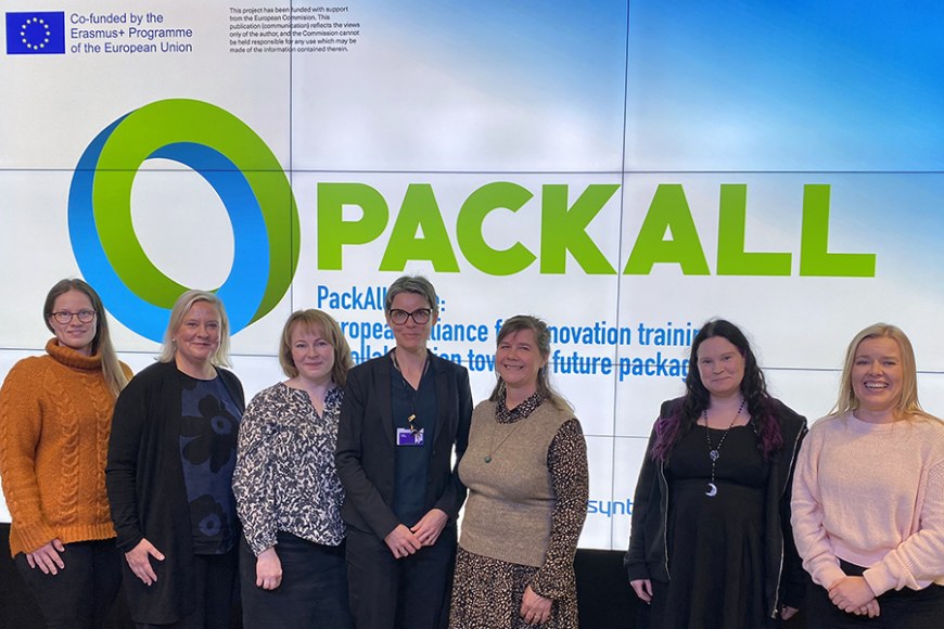 Ryhmäkuva hymyilevistä ihmisistä, takana PackAlliance-logo.