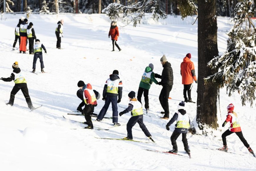 Lapset ulkoilemassa yhdessä hiihtäen, aikuiset ohjaavat heitä.