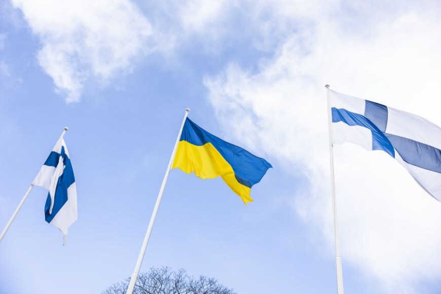 Three flags fly at half-mast. The blue and yellow flag of Ukraine in the middle. The blue cross flags of Finland on the edges.