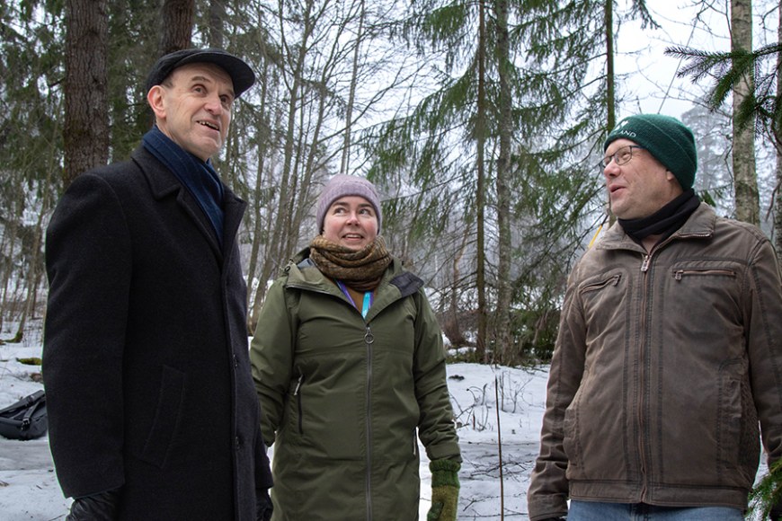 Kolme henkilöä seisoo lumisessa metsässä