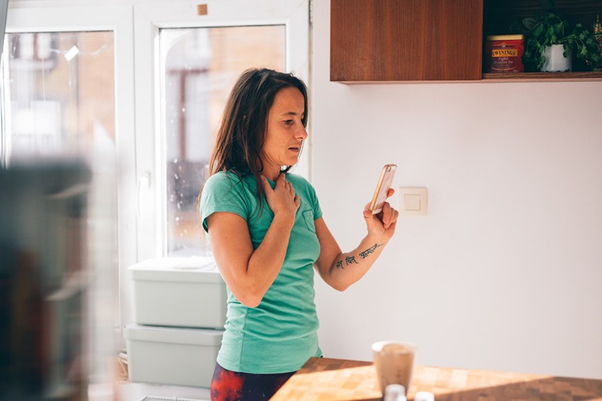A woman in green shirt holding a cell phone in a kitchen.