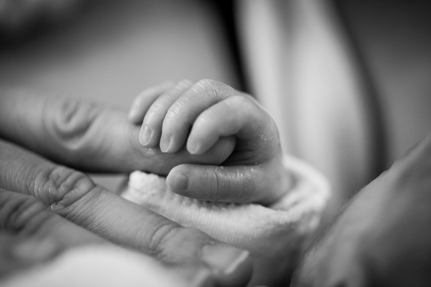 Vastasyntyneen vauvan käsi pitelee aikuisen sormesta.