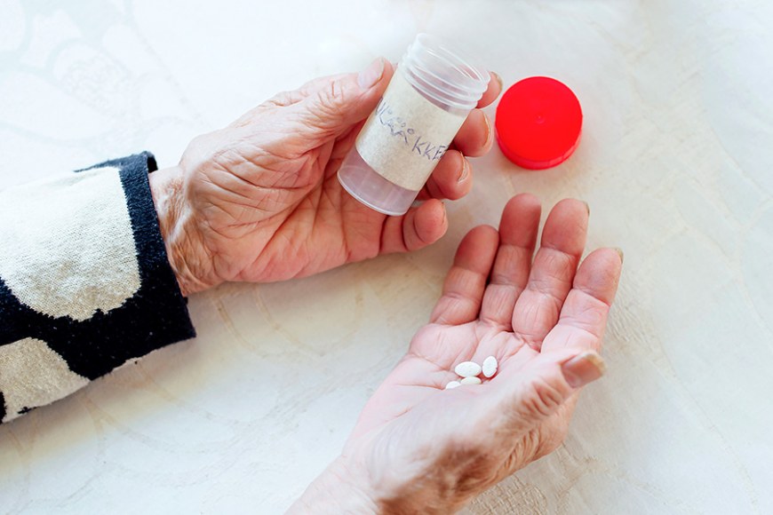 Vanhan ihmisen kädet, joissa toisessa on lääkepurkki ja toisessa kämmenelle kaadetut lääkkeet.