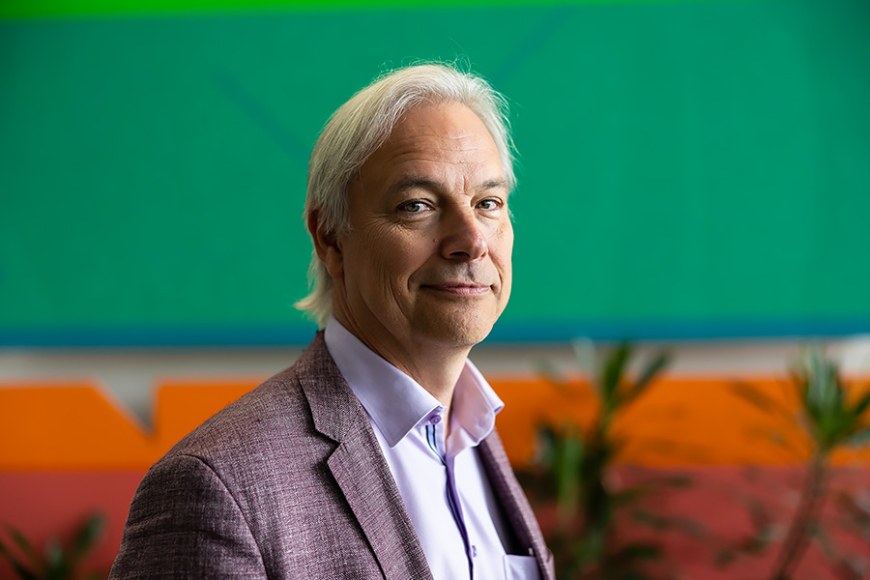 Portrait of Per Ashorn wearing a gray suit jacket. There is green plants and a green and orange wall in the backround.