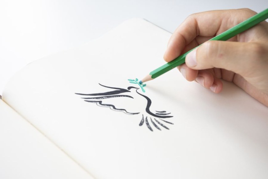 Henkilö piirtää vihreällä kynällä rauhankyyhkyn viereen lehvää.