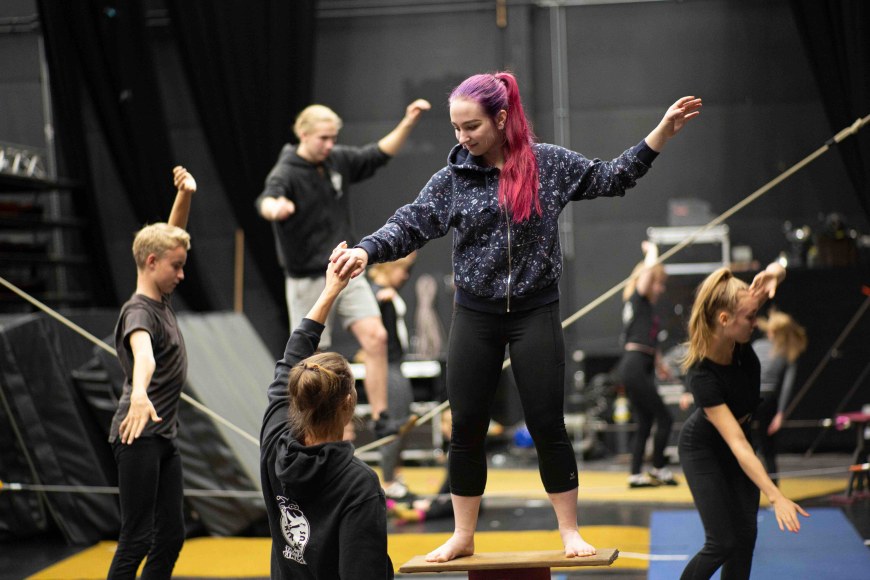 Sirkuskoulun opiskelijat harjoittelevat tasapainottelua ohjaajan avulla.