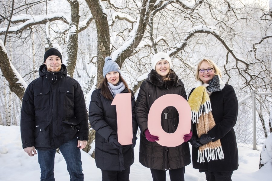 Four people standing in snow holding a sign that has the number 10 on it.