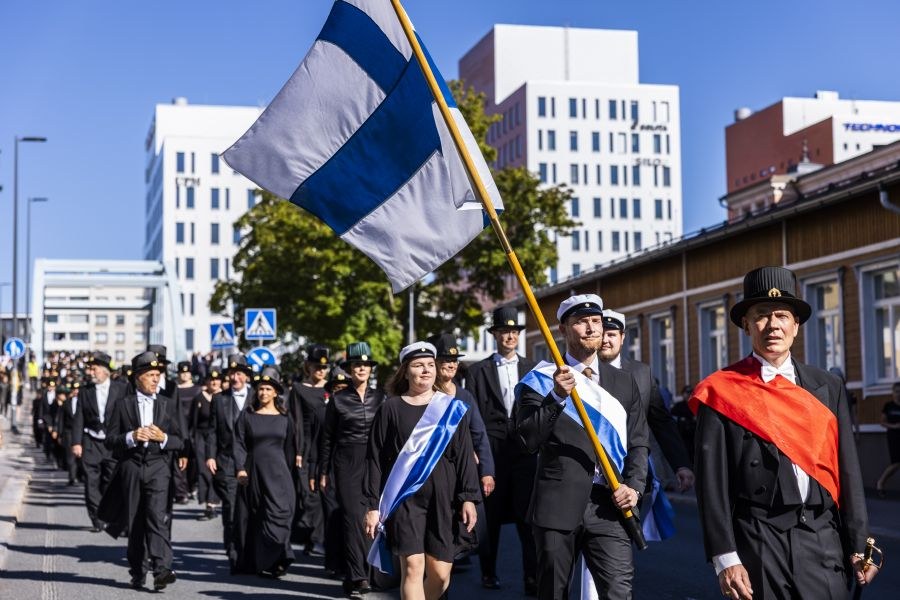 Kulkue kävelee kadulla, Suomen lippu liehuu.