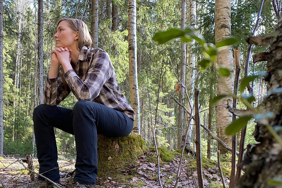 Matkailualan yrittäjä Maire Ylä-Tuuhonen istuu kannolla metsässä.