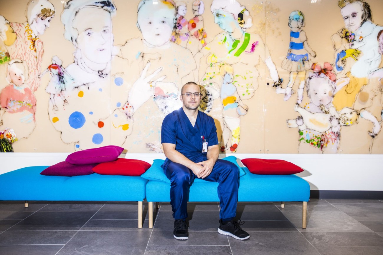 Jussi Hernesniemi istuu sinisellä sohvalla. Taustalla on seinä, johon on maalattu erilaisia ihmishahmoja.
