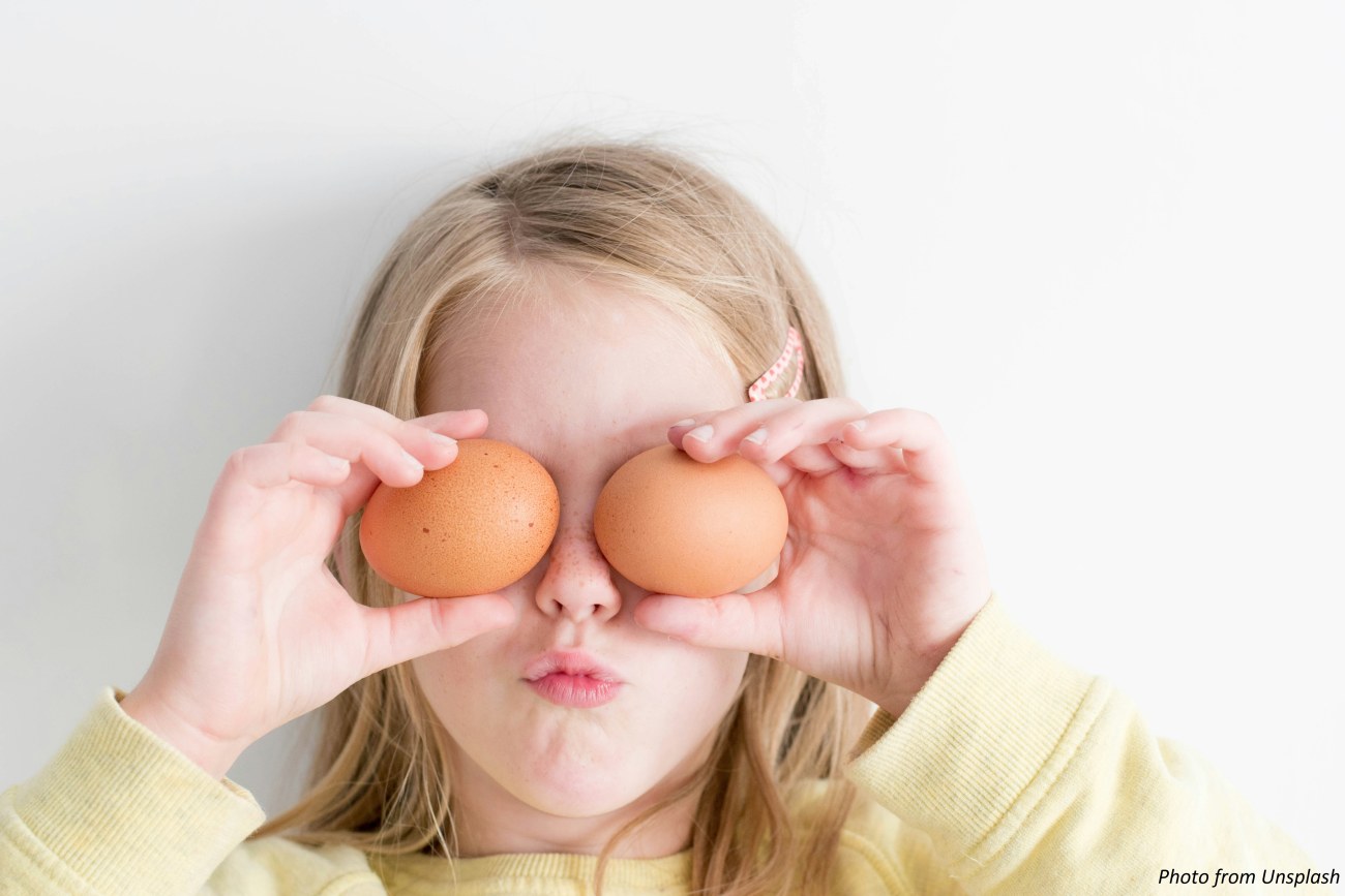 Tyttö on nostanut käsillään kaksi kananmunaa silmikseen.