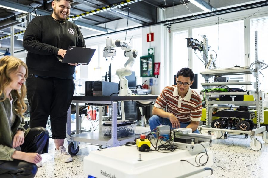 Three students in a lab, one standing, two in a squattin position.