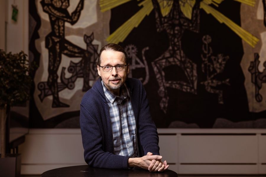 Anssi Männistö puolikuvassa, katse kameraan, kädet pöydällä rennosti päällekkäin.