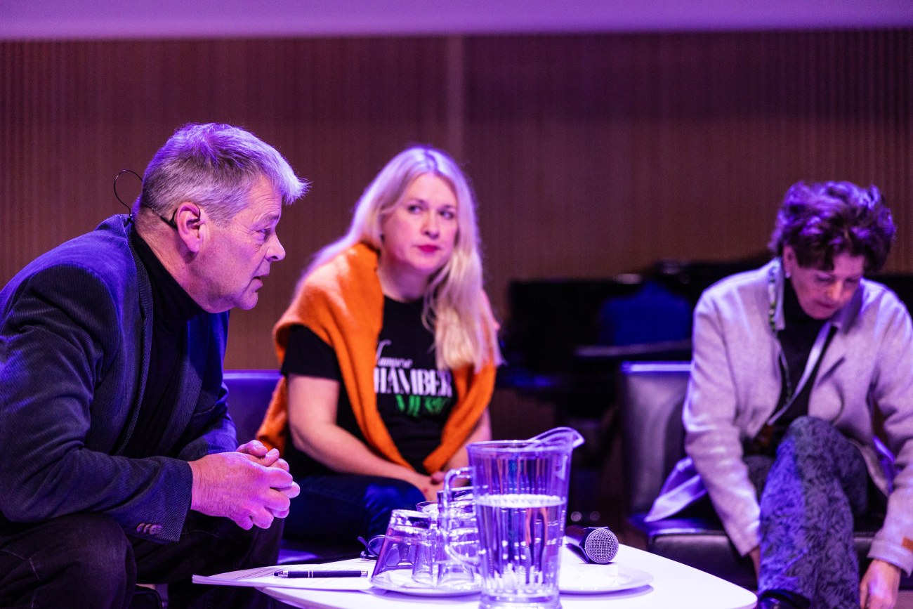 Kolme ihmistä istuu paneelikeskustelussa esiintymislavalla.