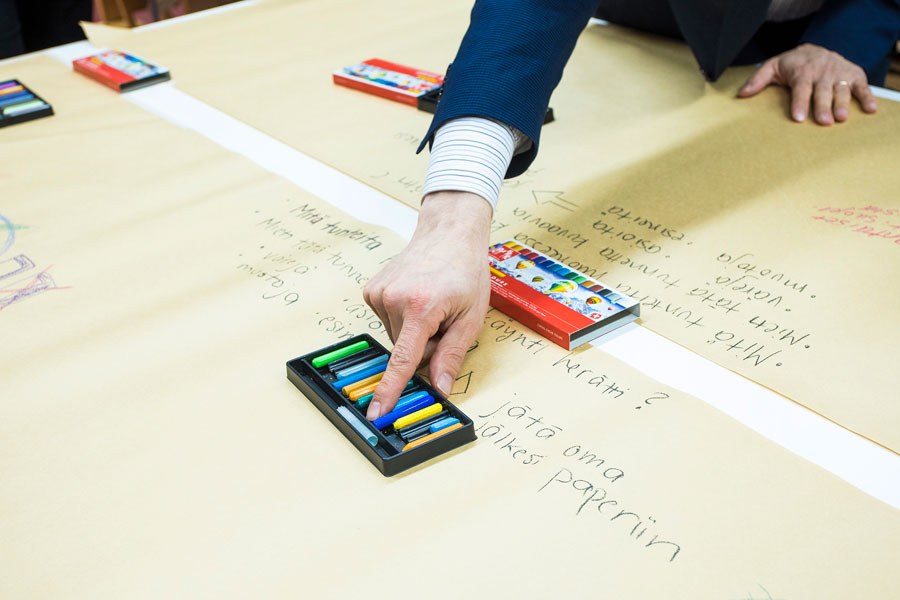 Piirtopaperi, jonka päällä on värikynälaatikko, johon henkilö osoittaa.