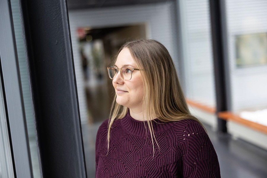 Henkilö viininpunaisessa neuleessa seisoo käytävässä, jossa on lasinen ulkoseinä.