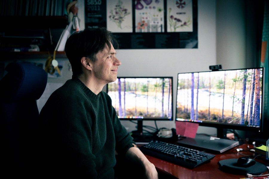 Vihreäpaitainen mies työpöydän ääressä katsoo tietokoneen ohi ulos ikkunasta.