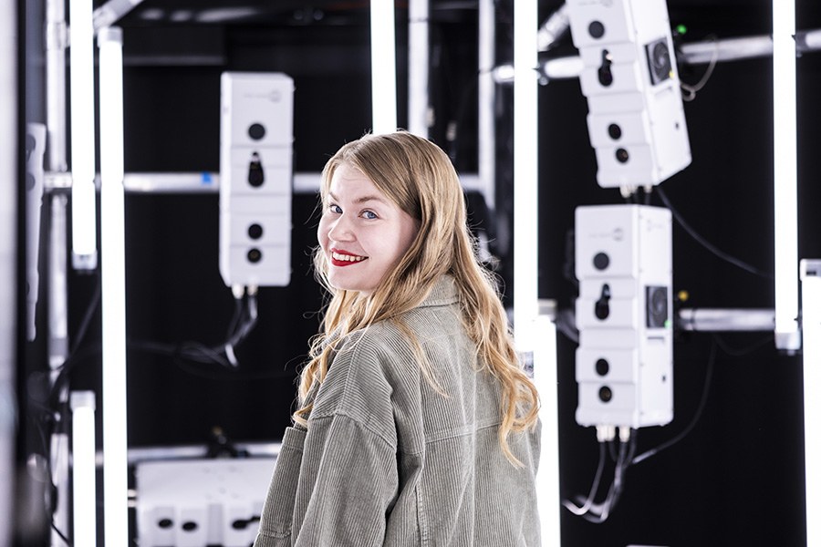 Opiskelija laboratoriossa laitteiden ympäröimänä katsoo kameraan.