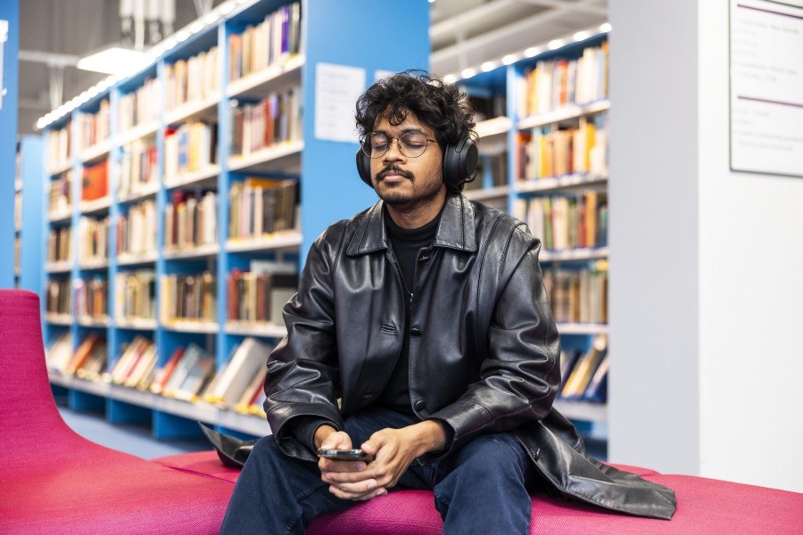 Henkilö istuu kirjastossa kuullokkeet päässään.