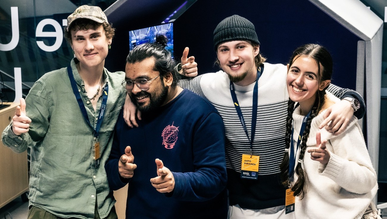 Neljä opiskelijaa kaulakkain näyttävät iloisena peukkua.