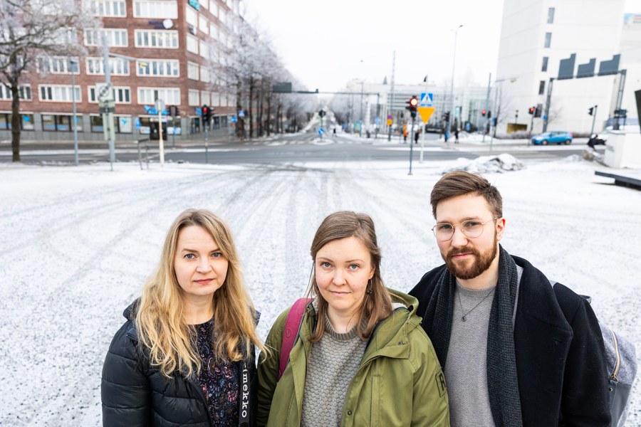 Kolme henkilöä seisoo ulkona talvisessa maisemassa, taustalla näkyy kaupunkia.