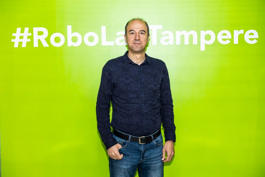 Mies seisoo vihreän seinän edessä ja katsoo kameraan.