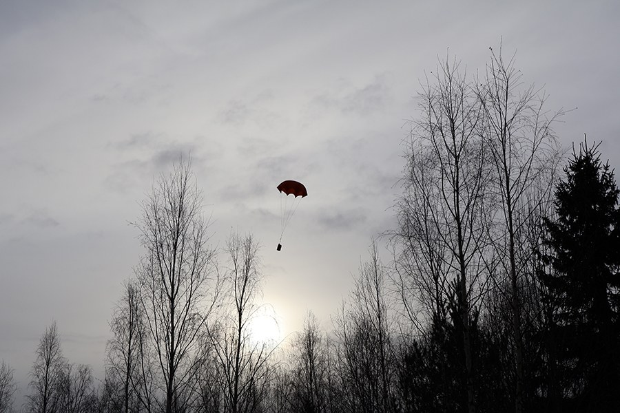 Drooni pudottaa laskuvarjon metsäaukealle. 