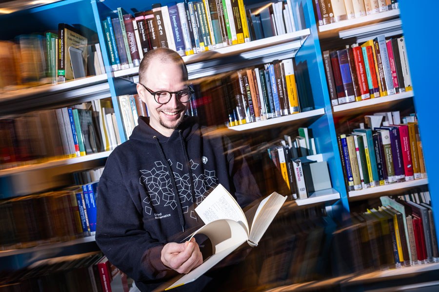 Professori Lassi Paunonen selailee kirjaa kirjastossa.