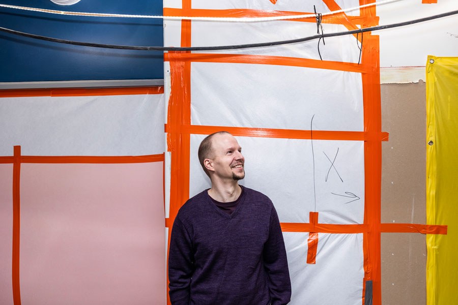 Lassi Paunonen katsoo poispäin kamerasta ja seisoo värikkään rakennustyömaaseinän edessä.