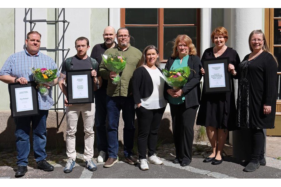 Palkintotauluja ja onnittelukukkia piteleviä henkilöitä rakennuksen edustalla. 