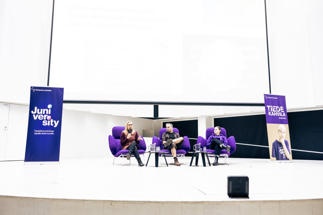 Keskustakampuksen juhlasalin lavalla istuu kolme henkilöä.