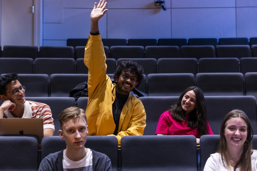 Opiskelija viittaamassa luentotilassa.