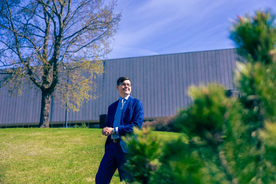 Janne Ruohonen is walking outside, with a university building, a lawn, and a tree in the foreground.