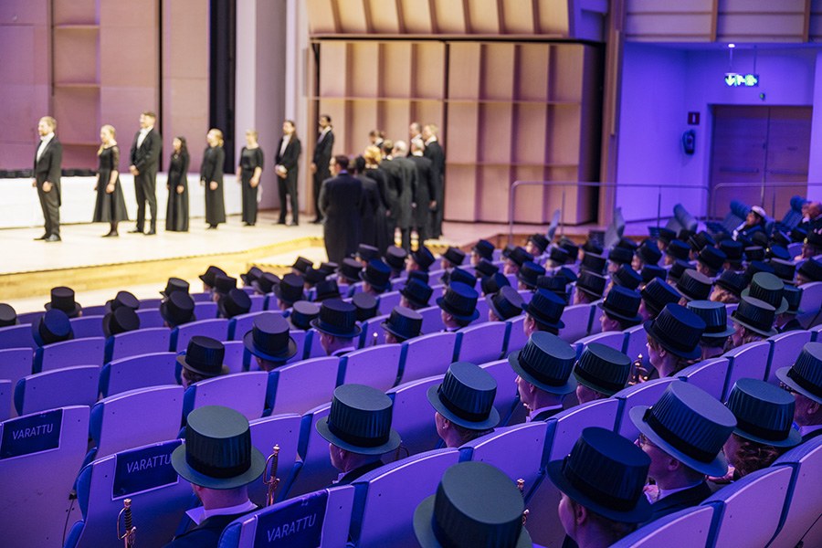 Promovoidut tohtorit istuvat penkkiriveillä, takana näkyy lavalle jonottavia promovoitavia