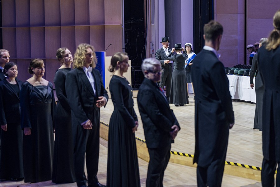 Tohtorit jonottavat lavalle promovoitavaksi, heidän takaansa näkyy parhaillaan promovoitava tohtori 