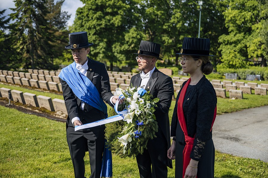 Kolme henkilö laskee seppelettä sankarihaudoille