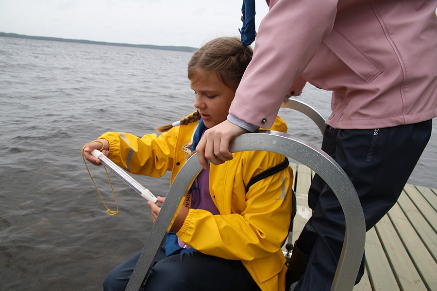 Lapsi tutkii veden lämpötilaa lämpötilamittari kädessä laiturilla.