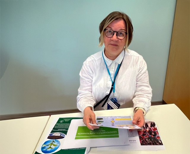 Pöydän ääressä istuva nainen pitää käsissään esitteitä.