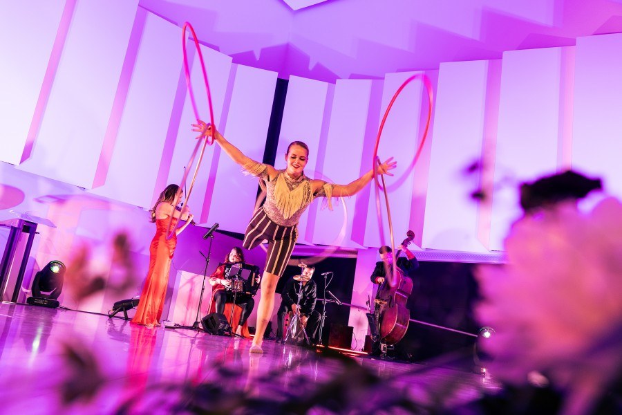 Nainen esittää sirkusakrobatiaa vanteiden kanssa esiintymislavalla. Taustalla pieni orkesteri.