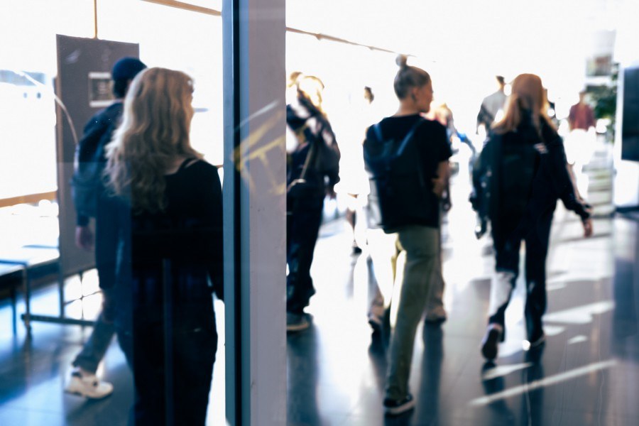 Muutama opiskelija kävelee eteenpäin. Kamera suuntaa heihin takaa.